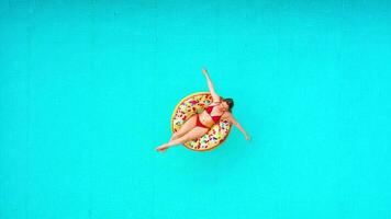 aéreo ver de un mujer en rojo bikini nadando en un rosquilla en el piscina video