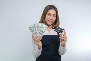mujer asiática en delantal posando con dinero en efectivo en dólares y tarjeta de crédito. foto