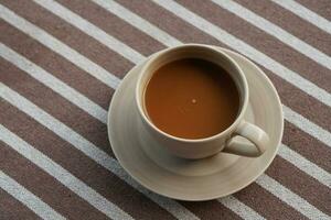 café en un cerámica taza y plata cuchara en un cerámica portavasos en marrón y blanco tela fondo, beber, alimento, salud, Copiar espacio foto
