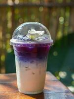 violet and white milk and white flower and ice , in a clear plastic glass, placed on a wooden table, on blur green leaf background, nature, food,drink photo