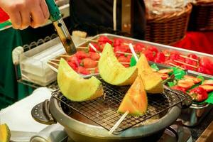 Hand of chef using burner cooking and burn slice of cantaloupes and melons on stove to sale for customer at Kuromon market. Cantaloupes Bar-B-Q is quaint and popular among tourists who come to Japan. photo