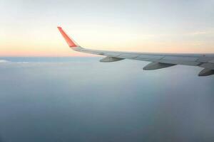 Outside window view of airplane with aircraft wing and sky of sunset background. photo