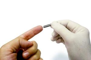 Hand of doctor in white medical glove holding blood lancet stab on human forefinger to check glucose in the blood isolate on white background and make with paths. photo