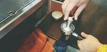 Close up barista's hand using tamper tool and grinder to make espresso shot in coffee maker machine at cafe in vintage tone . Making food and drinking. photo