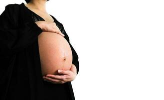 Asian Pregnant woman in black dress and holds hands on swollen belly isolated on white background and copy space with clipping path. Pregnancy 7-9 months, motherhood, love, expectation and care baby. photo