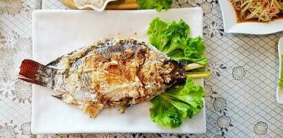 Salt-burning tilapia fish with green cabbage leaves on white dish at Thai restaurant. This food cook by grilled with ingredients of Thai herb inside food. Asian and Healthy life style eating. photo