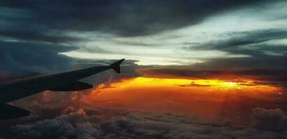 Silhouette of aircraft or airplane wing on dark sky with sunset light flare background. Transportation, Travel and Beauty of Nature concept photo