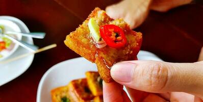 Close up hand holding deep fried minced pork or chicken toast with sliced onion and cucumber. Eating Asian food, Snacks and Fry bun in Thai style with sweet sauce. Delicious meal before lunch time. photo