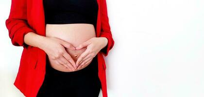 cerca arriba embarazada mujer en rojo traje formando un forma de corazón con su manos terminado su estómago o barriga aislado en blanco antecedentes y Copiar espacio con recorte camino. el embarazo 7-9 meses, maternidad foto