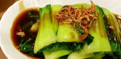 Close up Stir Fried Kale Hong Kong in oyster sauce with fried Shallots on top in white dish at Chinese restaurant. Asia food and Tasty plate photo