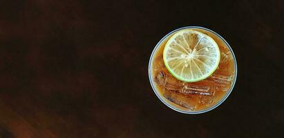 Top view or flat lay of plastic glass of iced lemon tea with sliced lime or lemon on top isolated on dark wooden background or table with left copy space - Refreshment drinking and Healthy drink photo