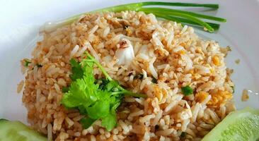 Close up Crab meat fried rice with slices cucumber, coriander and spring onion or scallion on white dish for lunch time. Asian food photo