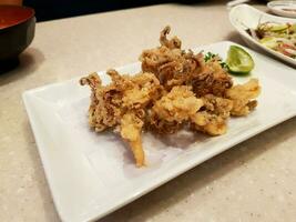 Deep fried squid with sliced lime or lemon in white dish on table at Japanese restaurant. Snack food and Seafood. photo