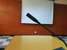 Black Microphone on wooden desk for talking or presentation in conference or meeting room with white projector board blurred background. Device and Tool photo