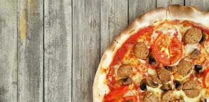 Pepperoni pizza on grunge gray wooden background or table with left copy space. Cooking ingredient with tomato, mushroom and Thai sausage. This food baked by use charcoal stove. photo