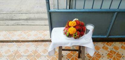 Fresh garland flower with rambutan, dragon fruit and glass of water on table with blue stainless steel fence and colorful tile background with copy space photo