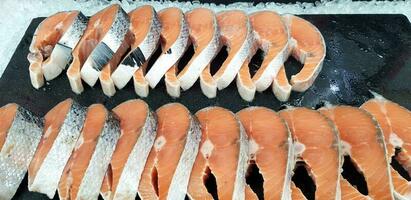 muchos Fresco rebanado de salmón en negro bandeja poniendo en hielo para cliente comprar y rebaja a pescado mercado foto