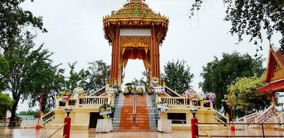 Pathum Thani, Thailand - May 16, 2023 Beautiful Thai crematory for funeral with flower decoration and tree in temple after raining day. Traditional, Culture and Exterior design of Building photo