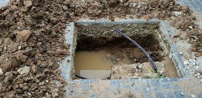 Hole for installation pillar or pole on cement ground with water and black wire cable at construction site and no strict and make symbol to tell danger area. Unsafe, Safety and structure photo