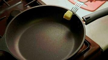 A piece of butter melts in a scratched preheated pan. Senior woman smears it with fork. video