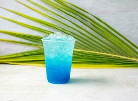 bebida hawaiana azul en un vaso de plástico y hojas de coco. foto