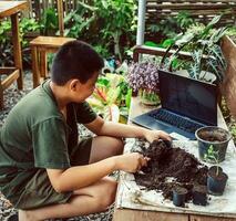 Boy learns to grow flowers in pots through online teaching. shoveling soil into pots to prepare plants for planting leisure activities concept photo