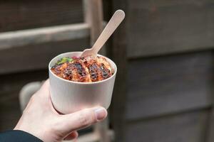 Hand holding a small cup of Japanese eel grilled with rice or unagi don photo