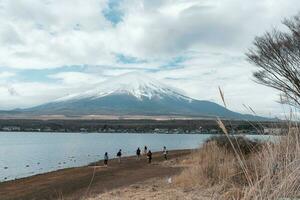 turista caminando en el apuntalar de yamanaka lago con monte. fuji antecedentes en nublado día foto