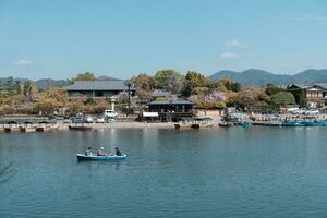 KYOTO, JAPAN - April 4, 2023 Tourists rowing boat in Katsura River in Arashiyama district with cherry blossom in spring time photo