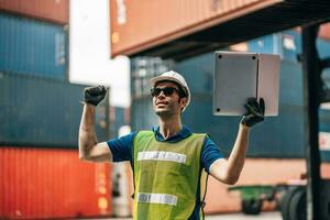 Engineer dock worker in protective safety jumpsuit uniform and with hardhat and use laptop computer at cargo container shipping warehouse. transportation import,export logistic industrial photo