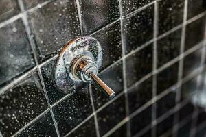 Closeup of modern black shower bath with chrome valve or faucet in bathroom in model home, apartment or house, tiles. Water droplets on shower wall photo