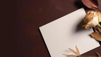 Top View of Blank White Paper, Rose Flower, Dried Leaves on Brown Background. Wedding Card and Space for Your Message. . photo