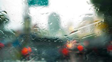 gotas de lluvia en el parabrisas de un coche conducción a lo largo el calle en un soleado tarde foto