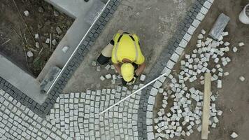 granito ladrillo pavimentación por caucásico construcción industria obrero. aéreo vista. video