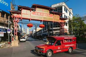 A red truck pass by the Chinese welcome gate of Chinatown, the oldest trading quarter of Chiang Mai in Thailand, features several markets and little side alleys with many shops. photo