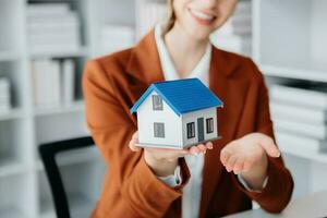 Young real estate agent worker working with laptop and tablet at table in office and small house beside it. photo