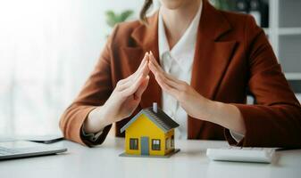 Female real estate agent is use hands to protect red roof for the concept of real estate investment about house trading, purchase at desk in office photo