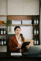 Asian businesswoman working in the office with working notepad, tablet and laptop documents photo