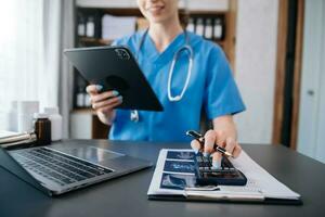 Healthcare costs and fees concept.Hand of smart doctor used a calculator and smartphone, tablet for medical costs at hospital in morning light photo