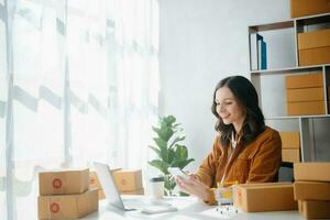 Young business owner woman prepare parcel box and standing check online orders for deliver to customer on tablet, laptop Shopping Online concept. photo
