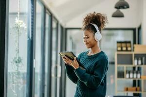 joven africano mujer escuchando música desde auriculares y escritura Nota para su trabajo idea en diario libro.ella en hogar oficina foto