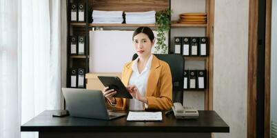 Young beautiful woman typing on tablet and laptop while sitting at the working wooden table office photo