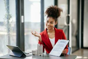 Young real estate agent worker working with laptop and tablet at table in office and small house beside it. photo