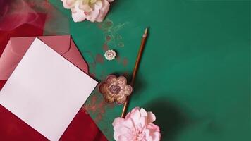 Flay Lay Blank Invitation Card Envelope with Floral, Pen on Red and Green Abstract Background. . photo