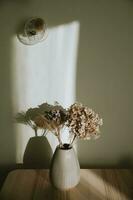 minimalista todavía vida con hermosa ramo de flores de seco flores en rosado cerámico florero en de madera mesa en tarde forma de ligero foto