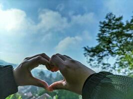 Hands of a woman in the shape of a heart with a finger and green nature background. A love concept with a sky background and space for text. Feelings and emotions concept. photo