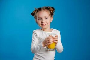 retrato de un pequeño niña de eslavo apariencia Bebiendo naranja jugo en un azul antecedentes foto