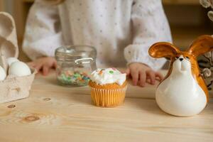 Cute little girl in a cotton dress at home in a wooden kitchen prepares an Easter cake photo