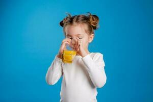 retrato de un pequeño niña de eslavo apariencia Bebiendo naranja jugo en un azul antecedentes foto