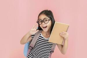 schoolgirl hugging book wearing backpack smiling isolated on pink background photo